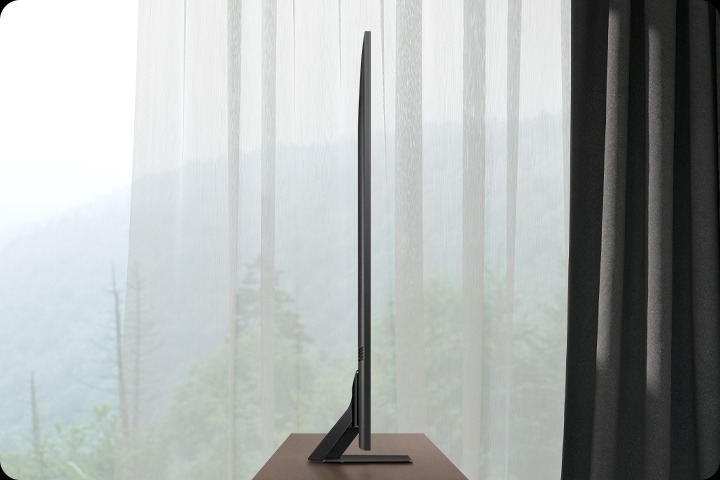 Новейший телевизор Samsung Neo QLED с его дизайном и подставкой One Connect гармонирует с окружающей мебелью в современной гостиной.